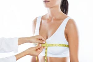 A doctor wrapping a tape measure around a woman’s breasts in preparation for a breast reduction surgery.